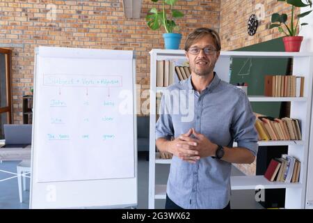 Kaukasischer männlicher englischlehrer, der Online-Unterricht neben Staffelei gibt Pad Stockfoto