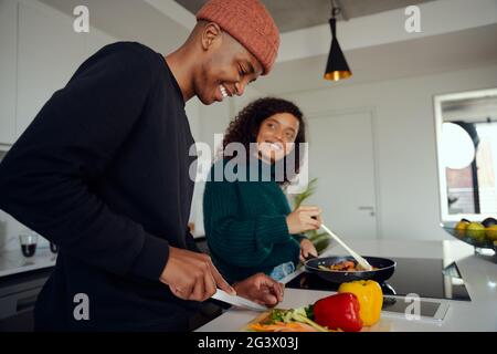 Junges gemischtes Rennpaar, das in der Küche zu Hause kocht. Glückliches Paar, das Essen zubereitete und lächelte. Hochwertige Fotos Stockfoto