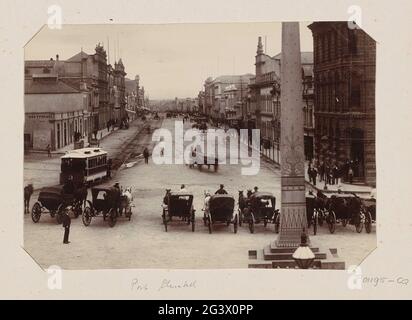 Hauptstrasse in Port Elizabeth mit Koetsiers, die im Vordergrund an einem Obelisken am Marktplatz warten. Teil des Fotoalbums von einer Reise der Vereinigten Staaten, Honolulu, Niederländisch-Indien, Aden, Sansibar und des südlichen Afrikas. Stockfoto