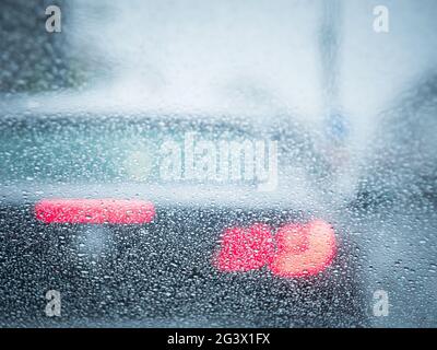 Die rote Hintergrundbeleuchtung eines Autos im Regen konzentriert sich auf Regentropfen Stockfoto