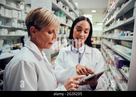 Senior Apotheker Lehre jungen Studenten, wie man das digitale zu verwenden Tablette, um Medikamente in der Apotheke zu finden Stockfoto