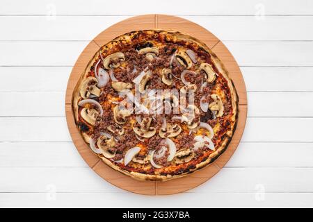Ganze Runde Pizza auf Holzplatte mit Pilzen, Zwiebeln und gehacktem Fleisch gekrönt. Draufsicht auf Whiteboard-Hintergrund Stockfoto