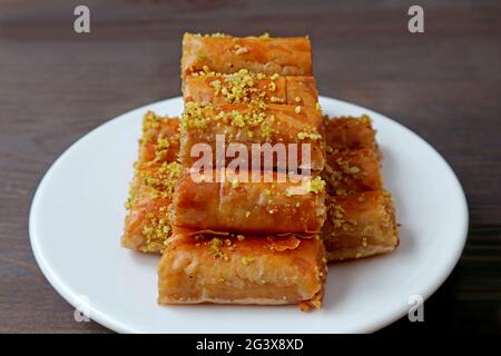 Teller mit Baklava-Gebäck, gekrönt mit gehackten Pistazien-Nüssen auf dem dunkelbraunen Holztisch Stockfoto