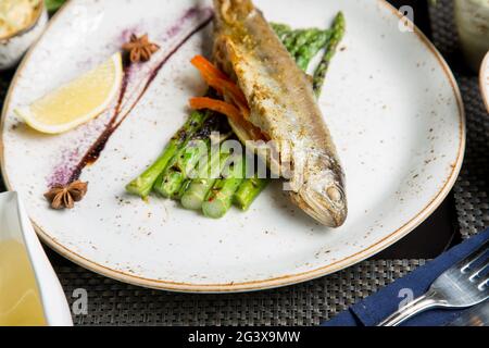 Ganze Kadaver der Meerforelle auf dem Grill. Gebratener roter Fisch mit Gemüse und Sauce. Nahaufnahme. Konzept - Essen, Delikatessen. Stockfoto