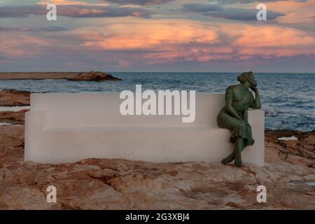 05-10-2021 Torrevieja, Alicante,Spanien Frau sitzt auf einer Bank am Meer und blickt auf den Horizont und wartet auf die Rückkehr ihres Fischers. Stockfoto