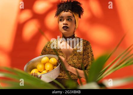 afroamerikanische Frau mit Metallschale und Zitronen auf Orange Stockfoto