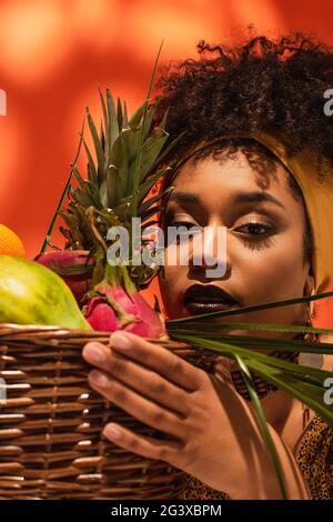 Porträt einer jungen afroamerikanischen Frau, die einen Korb mit exotischen Früchten auf Orange hält Stockfoto