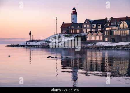 Winter in Urk mit Deich und Strand am Leuchtturm von Urk im Winter schneebedeckt, Sonnenuntergang am Leuchtturm von Urk Flevo Stockfoto
