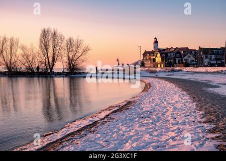 Winter in Urk mit Deich und Strand am Leuchtturm von Urk im Winter schneebedeckt, Sonnenuntergang am Leuchtturm von Urk Flevo Stockfoto