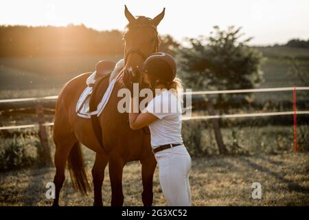 Junges Mädchen in den Strahlen der untergehenden Sonne küsst ihr Pferd.das Konzept der Liebe zur Natur. Hochformat. Lifestyle. Hochwertige Fotos Stockfoto
