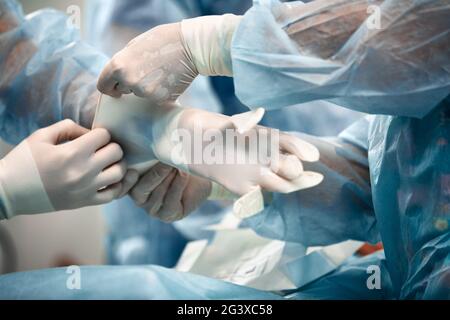 Krankenschwestern, die dem Chirurgen beim Anziehen eines Handschuhs im Operationssaal helfen, viele Ärzte in Handschuhe. Waschen von Handschuhen, Teil der Ausrüstung von Chirurgen Stockfoto
