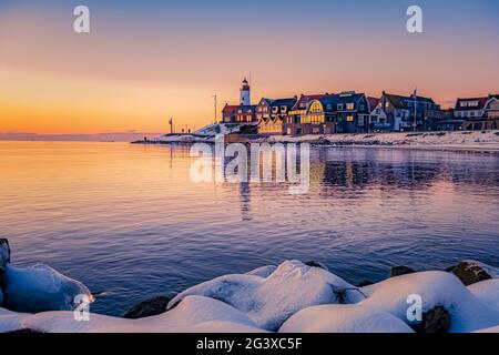 Winter in Urk mit Deich und Strand am Leuchtturm von Urk im Winter schneebedeckt, Sonnenuntergang am Leuchtturm von Urk Flevo Stockfoto
