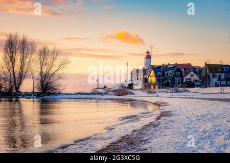 Winter in Urk mit Deich und Strand am Leuchtturm von Urk im Winter schneebedeckt, Sonnenuntergang am Leuchtturm von Urk Flevo Stockfoto