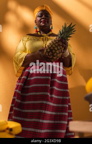 Low-Angle-Ansicht mittleren Alters afroamerikanische Frau verkauft Früchte mit Ananas in der Hand auf Orange Stockfoto