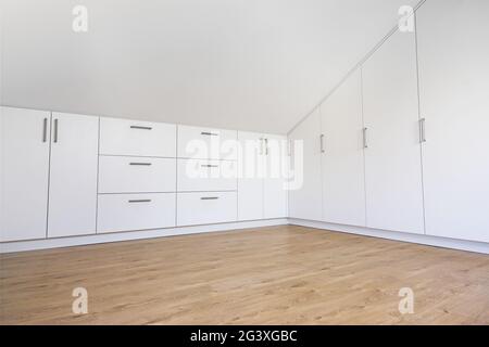 Moderner weißer Einbauschrank im leeren Raum mit schrägem Dach Stockfoto