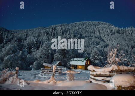 Kleines Haus in einer Winternacht mit glühenden Fenstern im Camping in den Bergen. Kleines Dorf in den Kaukasusbergen. Weihnachtsurlaub Stockfoto