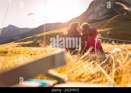 Das liebende Paar genießt den Sonnenuntergang in den Bergen und sitzt auf dem Boden. Warme Farben, alpen, Österreich Stockfoto