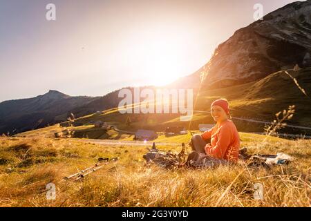 Wandermädchen genießt den Sonnenuntergang in den Bergen, sitzt auf dem Boden. Warme Farben, alpen, Österreich Stockfoto