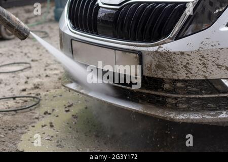 Autowäsche. Das Auto wird unter dem Druck eines Wasserstrahls gewaschen. Mit einem Wasserspray Schmutz von der Fahrzeugoberfläche abwaschen. Stockfoto