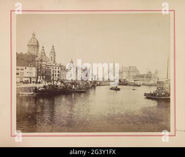 Blick auf die Prins Hendrikkade und die offene Havenfront mit der Nikolaikirche, dem Schreierstoren und rechts dem Hauptbahnhof von Amsterdam. Teil des Fotoalbums mit Aufnahmen von Sehenswürdigkeiten in Amsterdam. Stockfoto