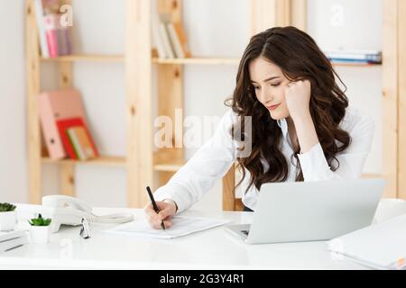 Junge hübsche Geschäftsfrau mit Notebook und Document in dem hellen, modernen Büro im Innenbereich Stockfoto