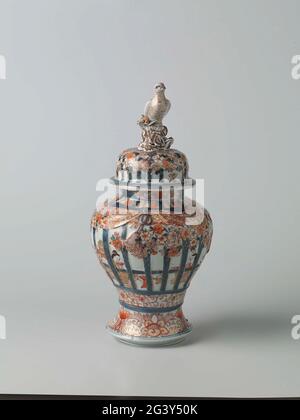 Bedecktes Baluster-Glas mit Figuren im Inneren hinter Rahmen, Prunus-Bäumen und Blumenrollen. Balusterförmige Deckeltopf aus Porzellan mit Spreizfuß, in Unterglasur blau und auf der Glasur rot, schwarz und Gold lackiert. An der Wand sitzen zweimal zwei Personen in einem Innenraum hinter einem gepflegten und bemalten Geländer. Dieses Geländer ist mit gepflegten und dekorierten prunus-Bäumen und Reifen mit Blumengetränken dekoriert. Unter dem Geländer eine Verbindung mit Blumengetränken. Eine Beziehung zu Lotusgetränken um den Fuß. Drei Kartuschen mit Lotusgetränken am Hals. Der Deckel mit der gleichen Dekoration; Deckel kn Stockfoto