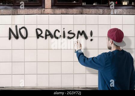 Person männlich schreiben mit Sprühfarbe kann die stoppen keine Rassismus Aussage an der Wand, Graffiti Symbol Konzept Stockfoto