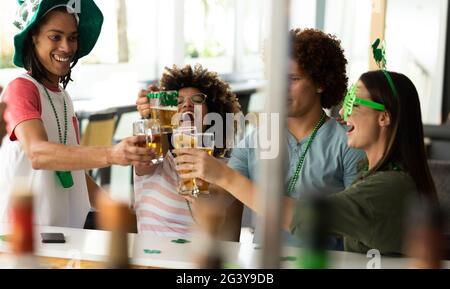 Eine bunte Gruppe von glücklichen Freunden, die St. patrick's Day Raising feiern Gläser Bier an einer Bar Stockfoto