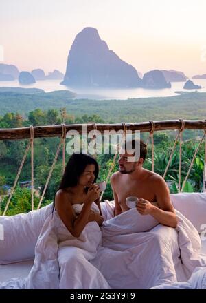 Phangnga Bay, Paar, das im Bett im Naturdschungel aufwacht und während des Sonnenaufgangs auf der Holzhütte in der mou über Ozean und Dschungel blickt Stockfoto