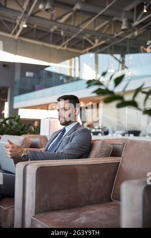 Nachdenklicher Geschäftsmann mit modernem Gadget, der alleine sitzt Stockfoto