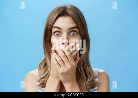 Nahaufnahme einer schockierten sprachlosen Frau, die den Mund mit gepressten Handflächen bedeckt und die Augen vor Überraschung und Sorge auf die Kamera knallte, keuchen Stockfoto