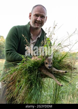 Magdeburg, Deutschland. Juni 2021. Wilko Florstedt vom Wildtierretter Sachsen-Anhalt trägt ein Rehkitz von einem Feld. Sie wurde zuvor mit einer Drohne verfolgt, die mit einer Wärmebildkamera ausgestattet war. Auf diese Weise werden die Rehkitze vor dem Tod durch den Mäher großer Landmaschinen geschützt. Nach eigenen Angaben hat der Verein Wildtierretter Sachsen-Anhalt in diesem Jahr bereits 200 Rehkitze vor einem qualvollen Tod gerettet. Quelle: Stephan Schulz/dpa-Zentralbild/ZB/dpa/Alamy Live News Stockfoto