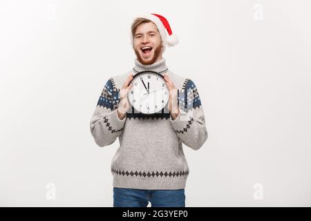 Urlaub Konzept - Junge glücklich aussehenden Bart Mann in Pullover Holding weisse Uhr über weiße studio Hintergrund. Stockfoto