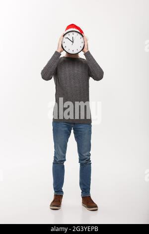 Urlaub Konzept - Junge stattlicher Bart Mann hinter weißen Uhr über weiße studio Hintergrund versteckt. Stockfoto