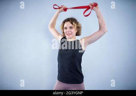 Sportlerin führt Übungen mit Widerstandsband. Menschen, Sport und Fitness. Junge Frau, die im Fitnessstudio mit Trainingsband trainiert. A Stockfoto