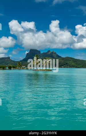 Zwei Palmen und eine Tiki-Skulptur auf einer kleinen Insel am Eingang zum Hafen des Flughafens Bora Bora (BOB) mit dem Berg Otemanu in der Ferne, Bora Bora, Stockfoto