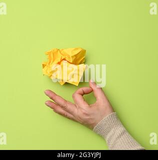 Gelber, zerknitterter Papierball und weibliche Hand auf grünem Hintergrund Stockfoto