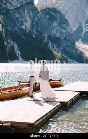 Die Braut und der Bräutigam laufen entlang einer hölzernen Bootsanlegestelle am Lago di Prags in Italien. Hochzeit in Europa, am Prags See. Frisch vermählt w Stockfoto