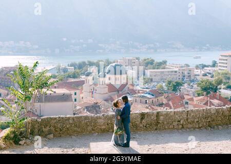 Die Braut und Bräutigam umarmen sich auf der Aussichtsplattform mit Ein malerischer Blick auf die Altstadt von Kotor und Die Bucht von Kotor Stockfoto