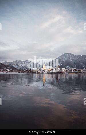 Blick über den winterlichen Tegernsee auf das Dorf Rottach-Egern mit der Kirche Sankt Laurentius, Bayern, Deutschland. Stockfoto