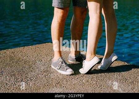 Die Beine eines Mannes und einer Frau in Sneakers, die sich auf dem Pier umarmt, stehen auf Zehenspitzen Stockfoto