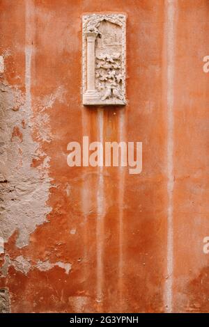Nahaufnahmen von Gebäudefassaden in Venedig, Italien. Steinrelief auf einer kleinen rechteckigen Steinplanke, auf einer orangefarbenen Wand auf dem fa Stockfoto