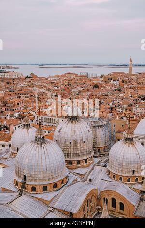 Blick von oben auf die St. Mark's Cathedral auf dem St. Mark's Square, mit einem großen Backsteinturm. Vor dem Hintergrund der gefliesten Orangendächer Stockfoto