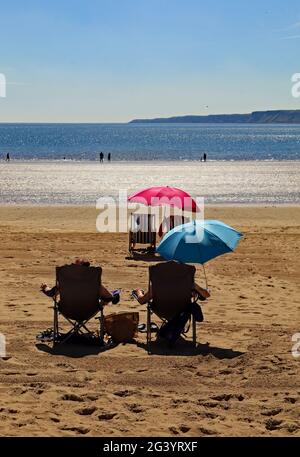 Sonnenbaden am Strand von Scarborough mit roten und blauen Sonnenschirmen zum Schutz vor der Sonne. Fragen Sie sich, ob sie unterschiedliche politische Ansichten haben Stockfoto