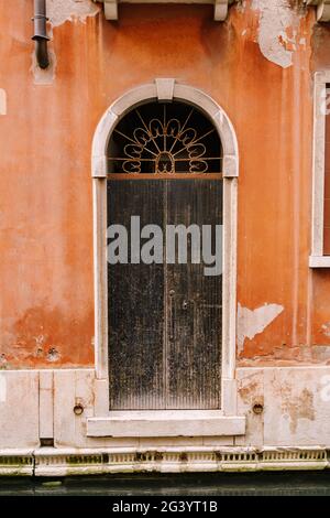 Nahaufnahmen von Gebäudefassaden in Venedig, Italien. Eine alte schwarze, zerkratzte Tür, in einer gewölbten Tür, mit einem rostig geschmiedeten Kühlergrill A Stockfoto