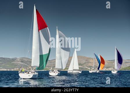 Segelboote konkurrieren bei Sonnenuntergang in einer Segelregatta, Rennen der Segelboote, Spiegelung der Segel auf dem Wasser, bunte Spinnaker, Anzahl Stockfoto