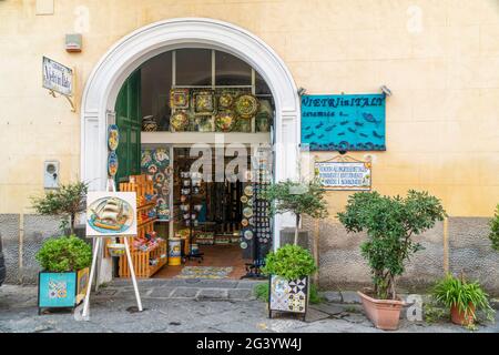 Vietri-Italien - 02.23.2019: Schöne Ansicht der Eingangstür des Souvenirshopfes. Grüne Blumen im Freien. Viele kunstvoll handgefertigte Teller hängen an der Wand Stockfoto