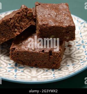 Gebackene quadratische Stücke Brownie Walnuss Schokoladenkuchen liegen auf einem runden Teller Stockfoto