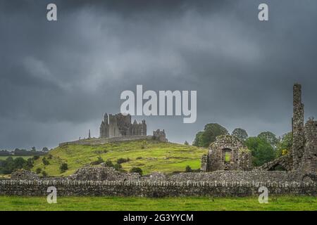 Der Felsen der Burg Cashel, der durch die alten Ruinen der Abtei von Hore mit einem dunklen, dramatischen Sturmhimmel gesehen wird Stockfoto