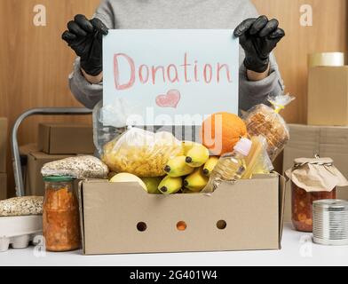 Frau in einem grauen Pullover und Handschuhen hält ein Blatt Papier mit der Aufschrift Spende Stockfoto